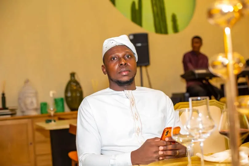 Un homme en tenue blanche, attablé, consulte son téléphone pendant un repas partagé.