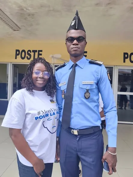 Une bénévole en tee-shirt de campagne pose aux côtés d'un agent de police devant un poste.