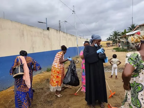 Groupe de participants nettoyant un terrain avec des balais et des sacs.